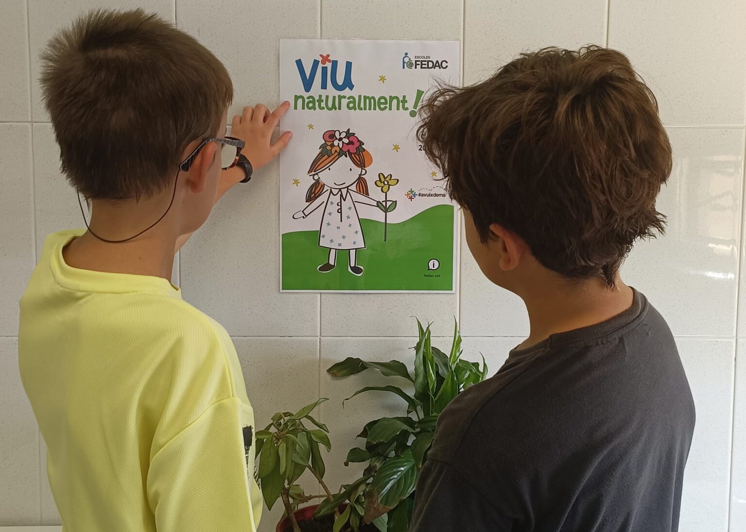 Alumnes de les escoles FEDAC descobreixen el cartell amb el lema del curs 2023-24, "Viu naturalment!".